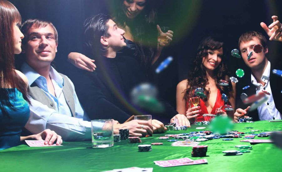 Vihreän pokeripöydän äärellä mies tekee rohkean panostuksen pelimerkeillä, kun ympärillä olevat naiset seuraavat jännittyneinä. Hymyilevät kasvot kertovat, että kaikilla on hauskaa pelatessaan pokeria ja nauttien jännittävästä pelikokemuksesta. 